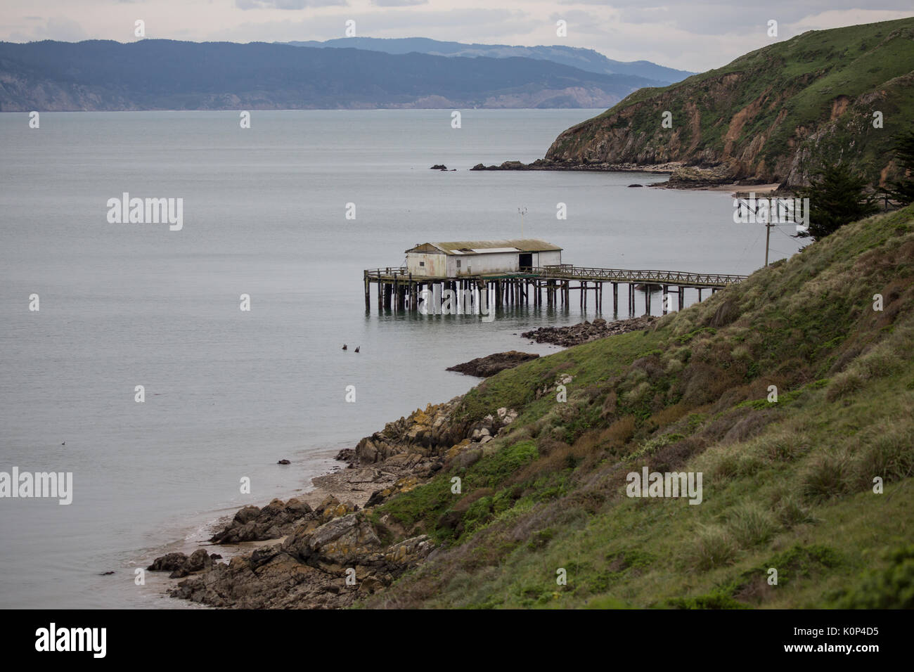 Fishing boat dock and processing shed juts out from rugged coastline at low tide Stock Photo