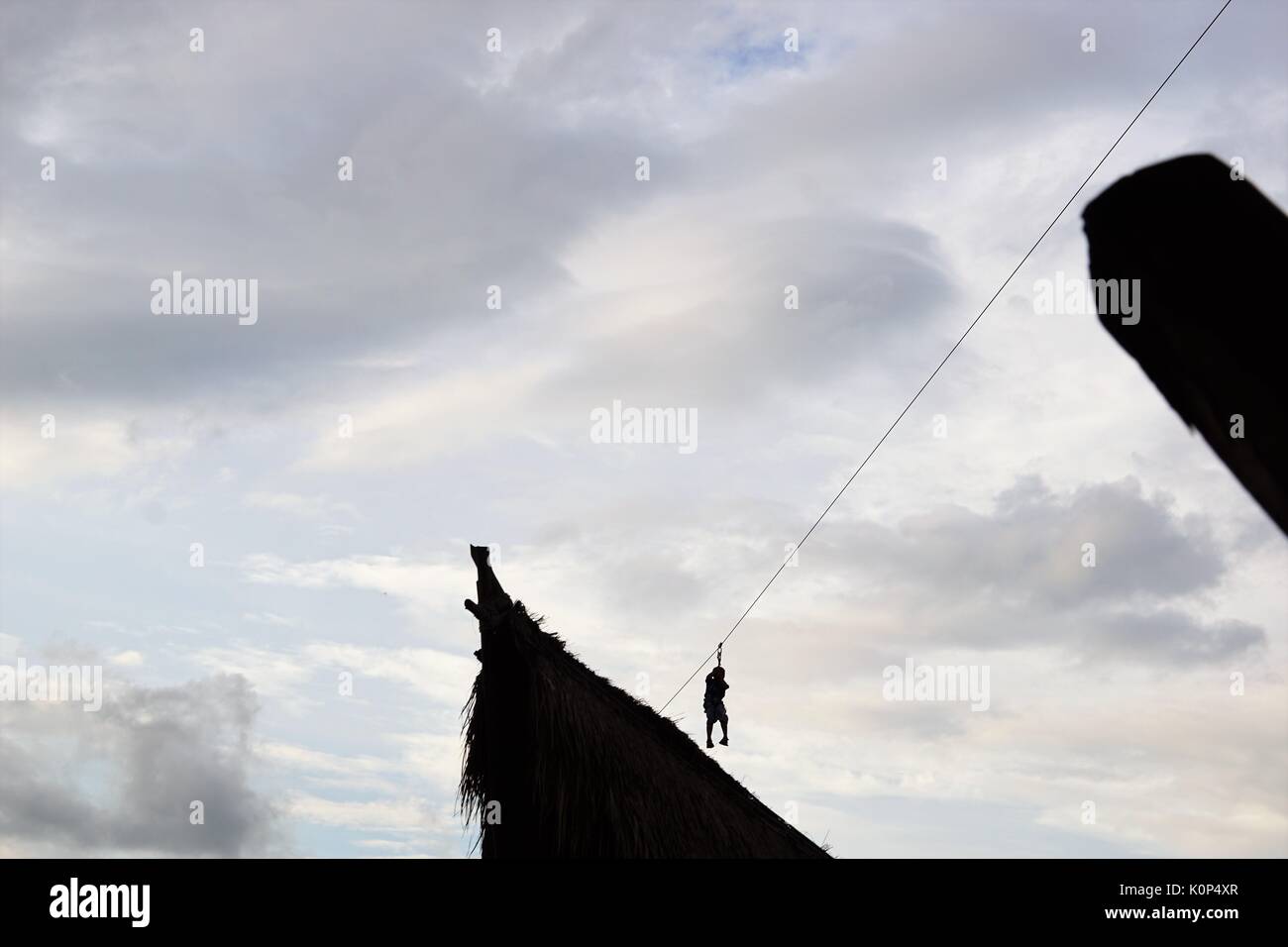 person zip lining between buildings against blue sky with clouds Stock Photo