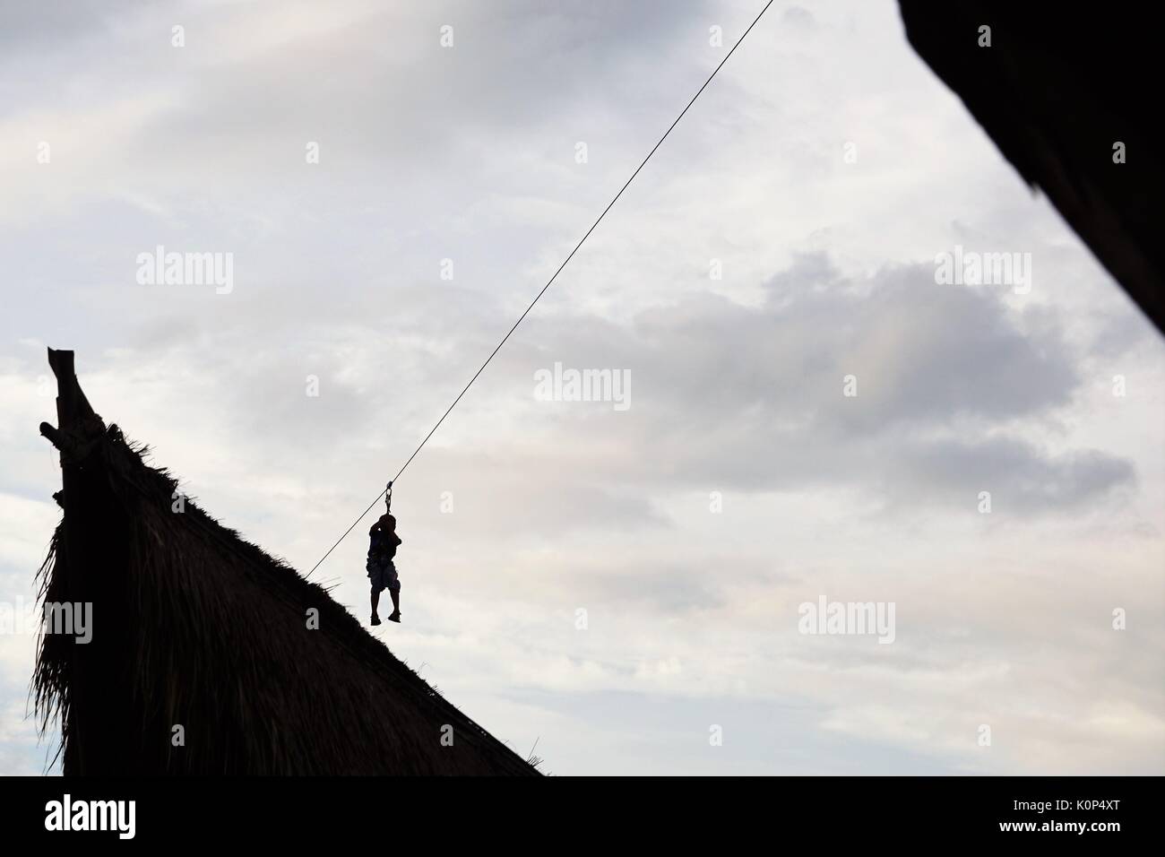 person zip lining between buildings against blue sky with clouds Stock Photo