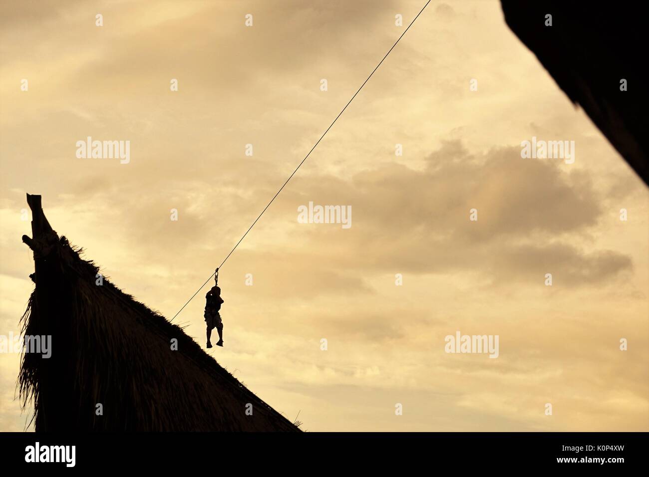 person zip lining between buildings against blue sky with clouds Stock