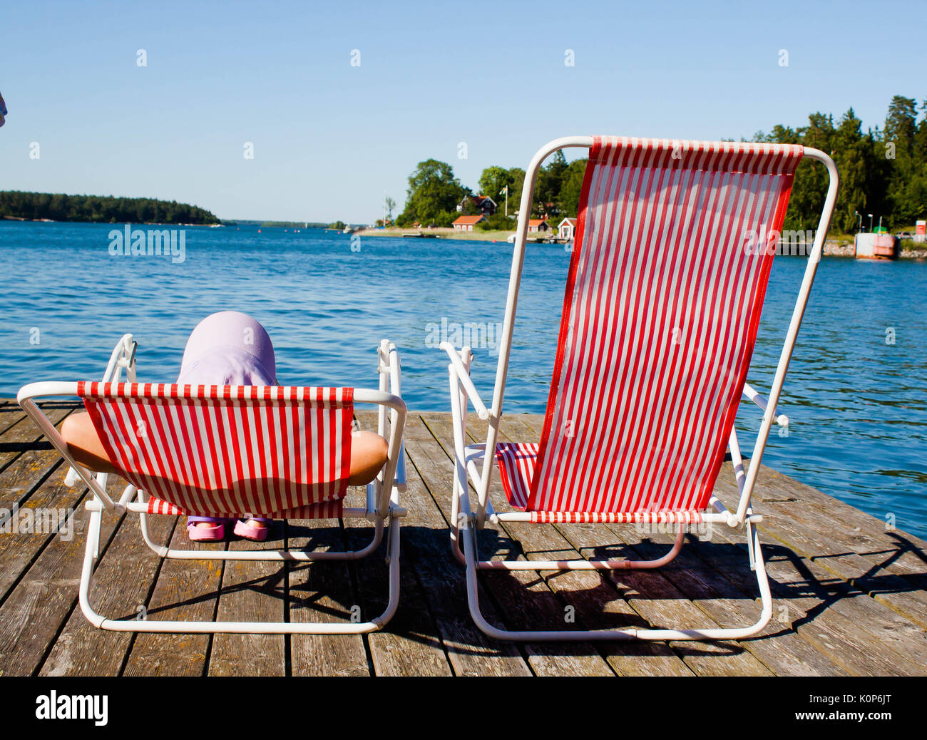 Girl sunbathing sitting on a hammock at the lake dock in summer Stock Photo