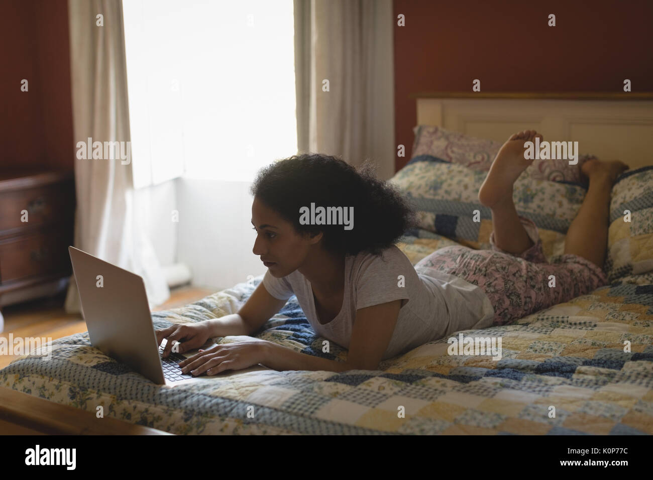Woman lying and using laptop on bed in bedroom Stock Photo
