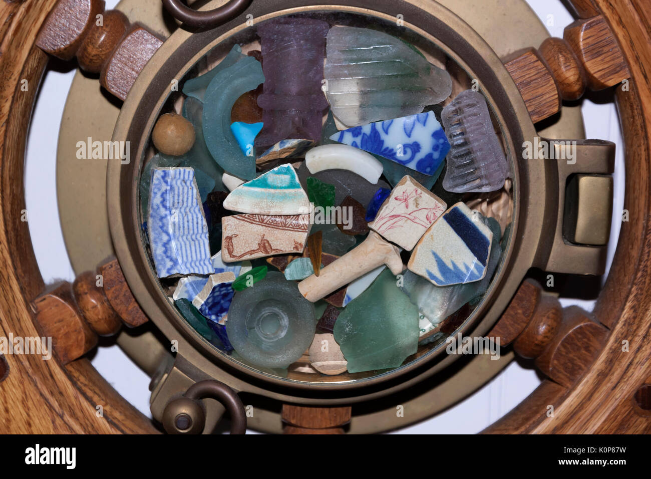Sea glass, cracked pottery, & found objects displayed under glass in a ship wheel. Stock Photo