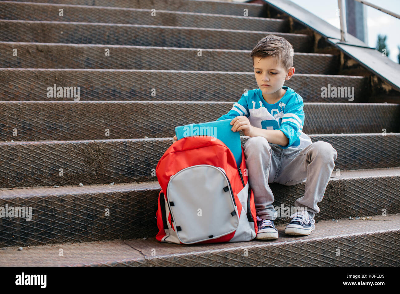 Unhappy young student sitting outside school and putting books in his ...
