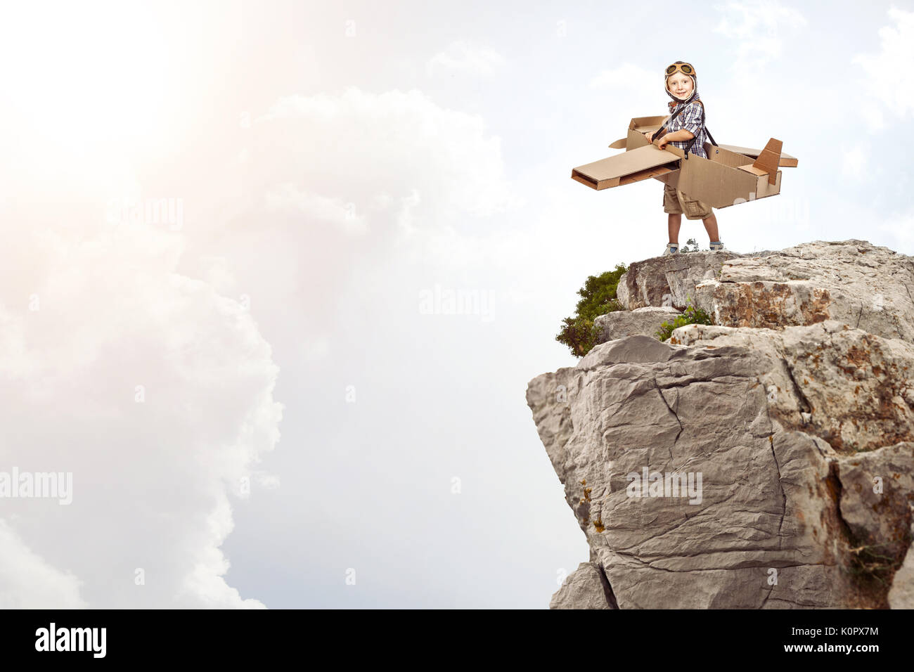 portrait of caucasian child play with cardboard airplane on cliff Stock Photo