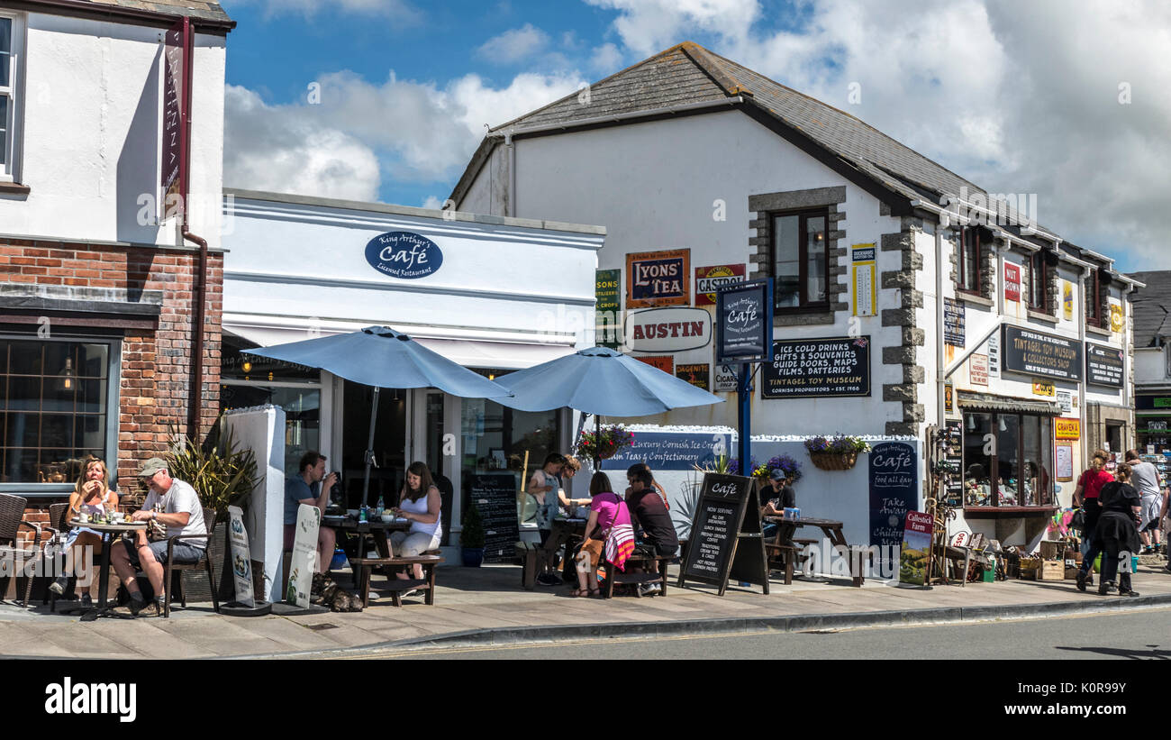 People sitting outside a cafe / restaurant, and others walking along Fore Street, in the small tourist town of Tintagel, Cornwall, England, UK. Stock Photo