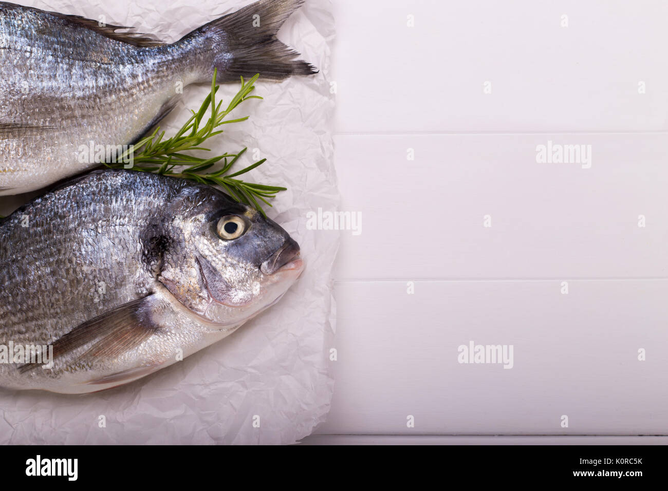 Fresh raw sea bream fish with lemon slices, salt, rosemary and olive ...