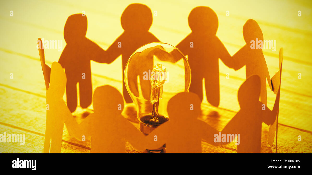 High angle view of blue paper figures standing around light bulb on wooden table Stock Photo