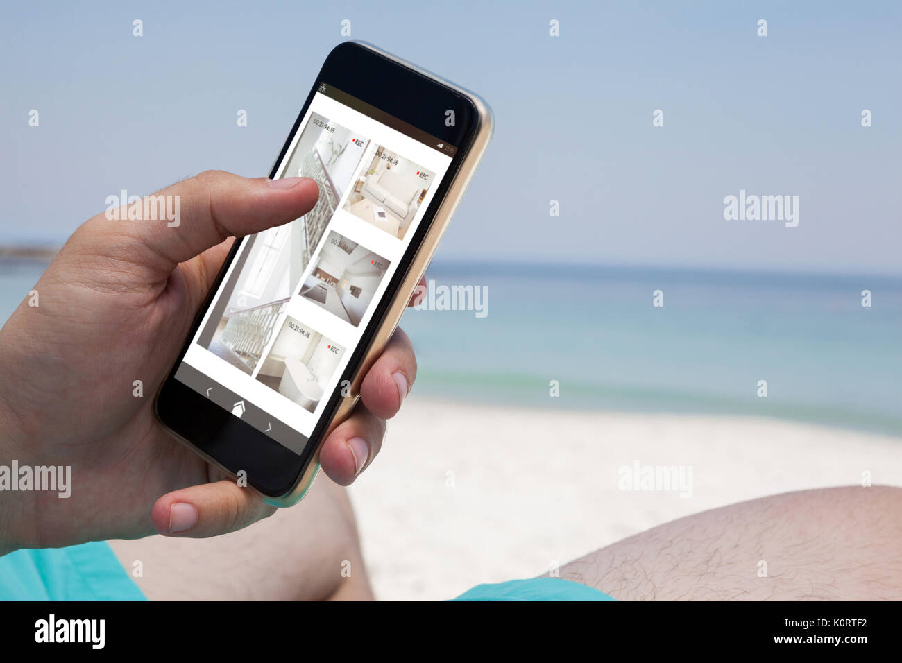 Interior of house on cellphone display against close up of man using smartphone at beach Stock Photo