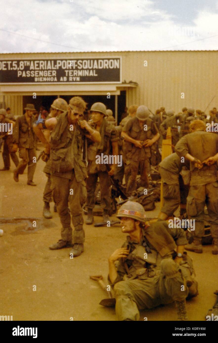 A large group of soldiers can be seen in their uniforms with full combat gear, doing their best to relax by socializing and smoking, awaiting transport, Bien Hoa Air Base, Vietnam, 1964. Stock Photo