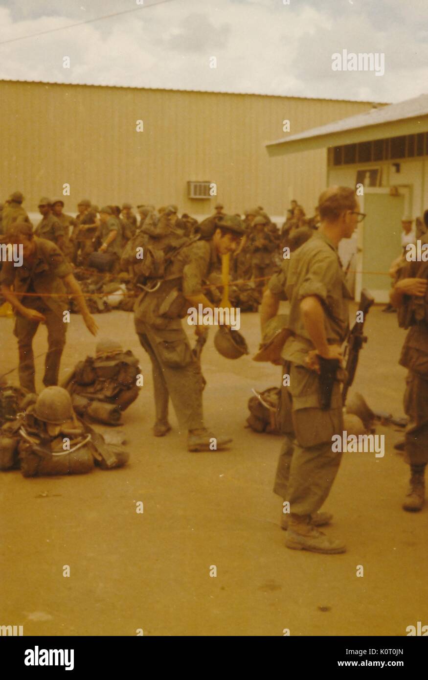 A large group of soldiers are gathered outside, in uniform with full combat gear, awaiting transportation, Bien Hoa Air Base, Vietnam, 1964. Stock Photo