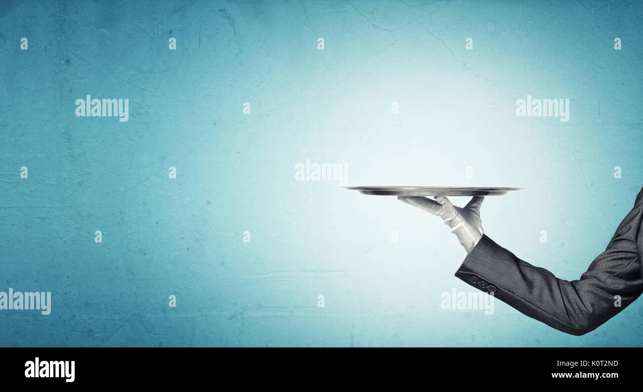 Hand of butler holding empty metal tray against blue background Stock ...