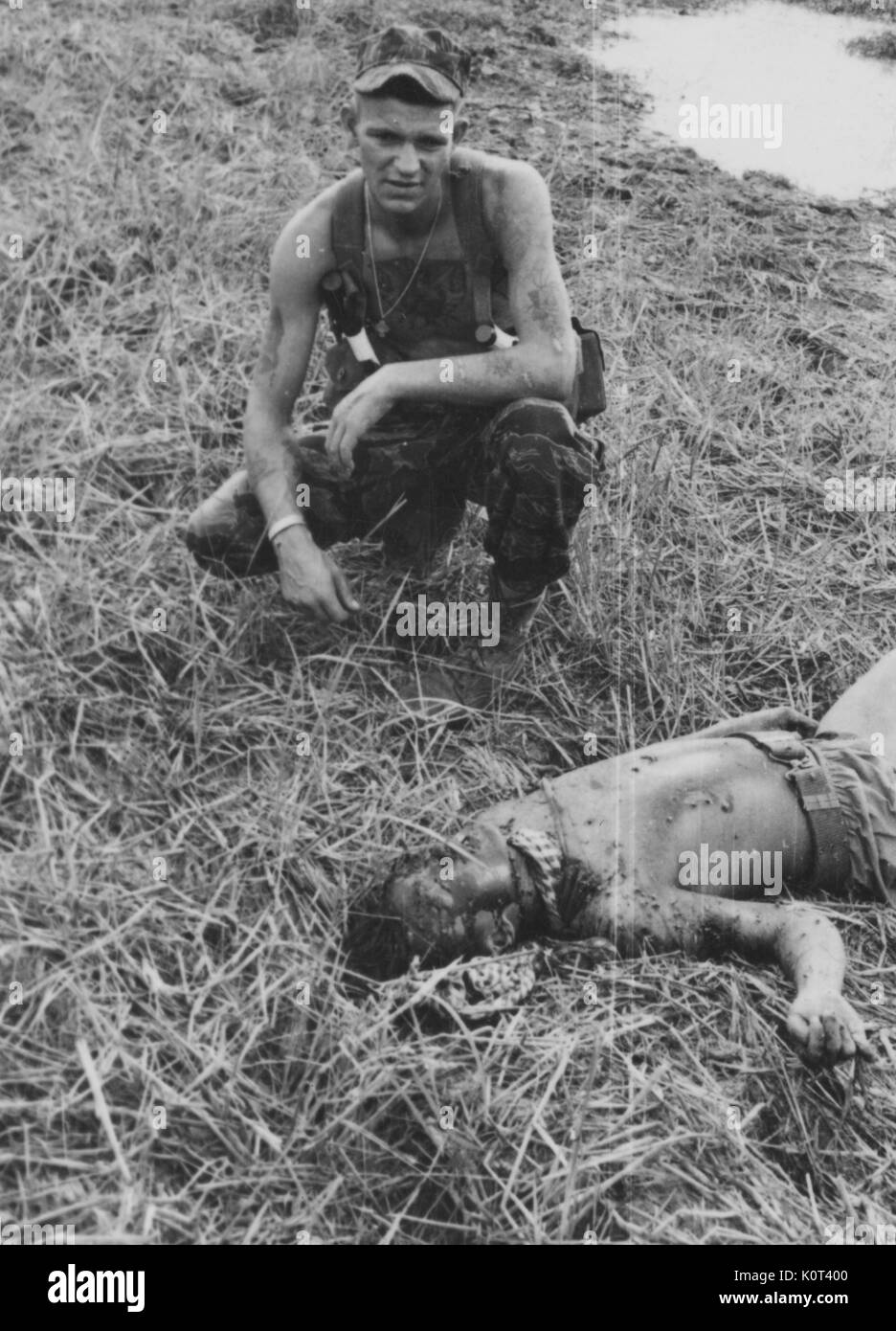 American advisor in uniform, in Vietnam, kneeling over the mutilated body of a dead Viet Cong soldier laid on a grassy field, early in the Vietnam War, WARNING: GRAPHIC, 1961. Stock Photo