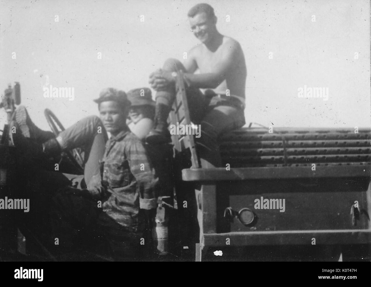 A photograph of two soldiers and aVietnamese personnel member sitting on a military truck, one of the soldiers is sitting on a pile of building materials in the bed of the truck, Vietnam, 1967. Stock Photo