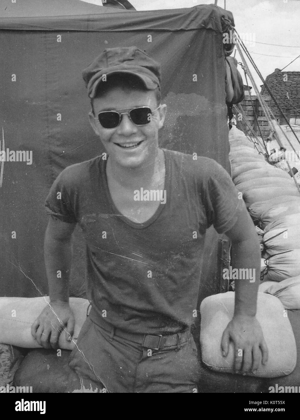 A photograph a United States Army serviceman wearing sunglasses and smiling while leaned back against a pile of sandbags, Vietnam, 1967. Stock Photo