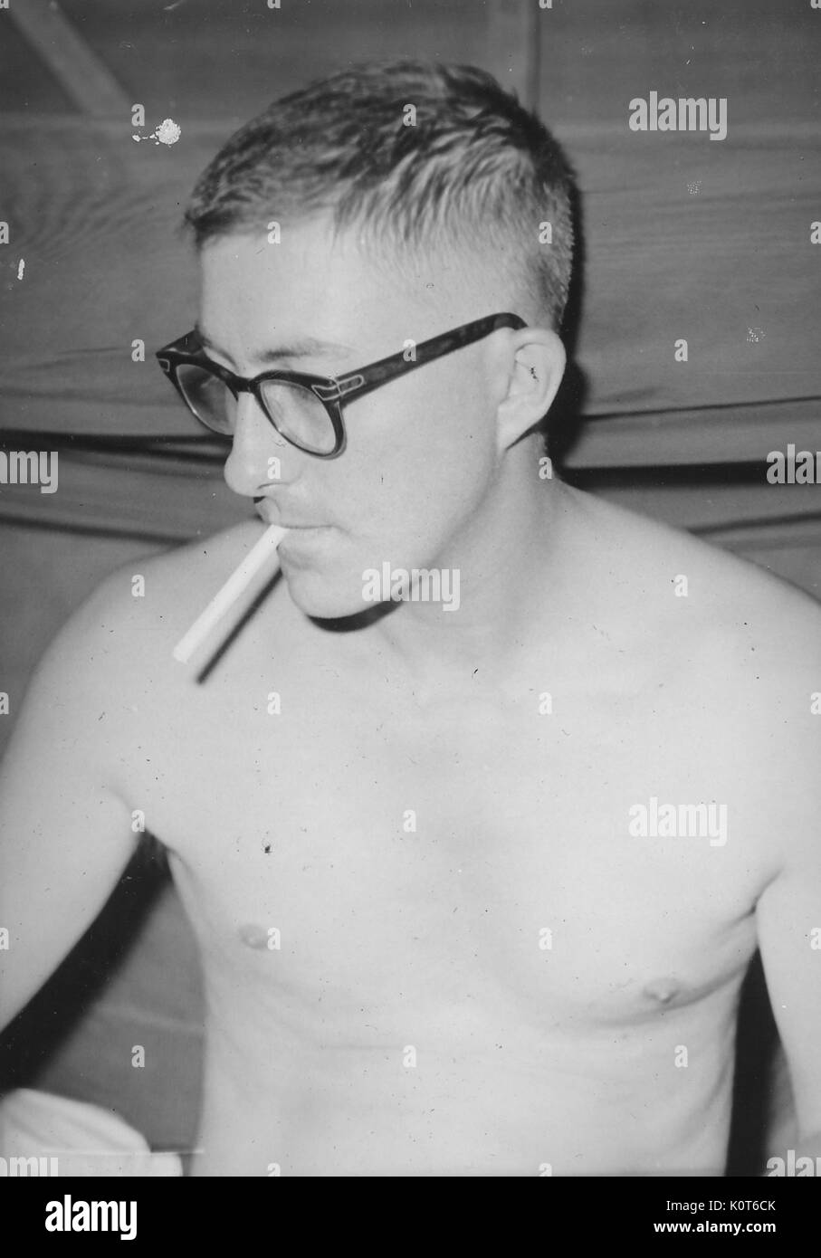Soldier smoking a cigarette without his shirt on, wearing military issue glasses, Vietnam, 1967. Stock Photo