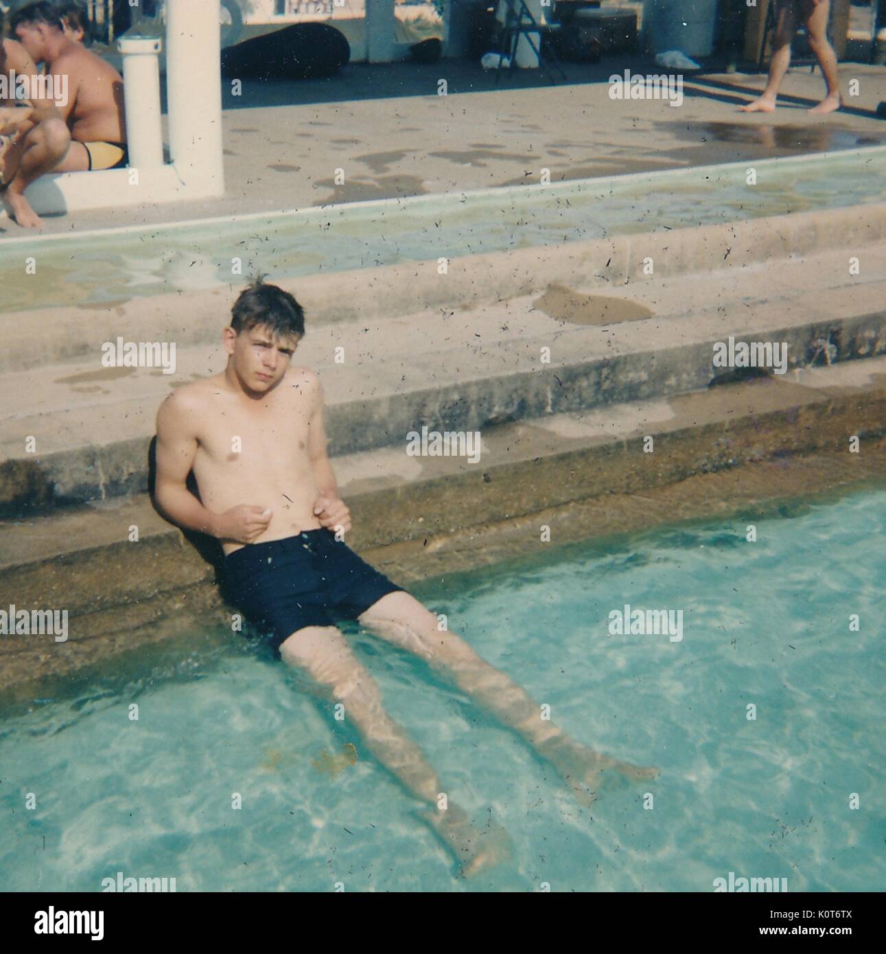 A United States serviceman relaxing at the edge of a swimming pool, other soldiers can be seen around the deck in the background, Vietnam, 1968. Stock Photo