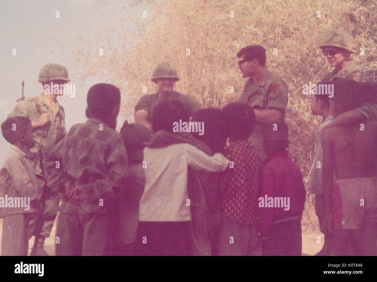 A photograph of a group of United States Army servicemen speaking to a group of Vietnamese children, the servicemen are all in their combat uniforms and one is carrying his rifle, Vietnam, 1968. Stock Photo