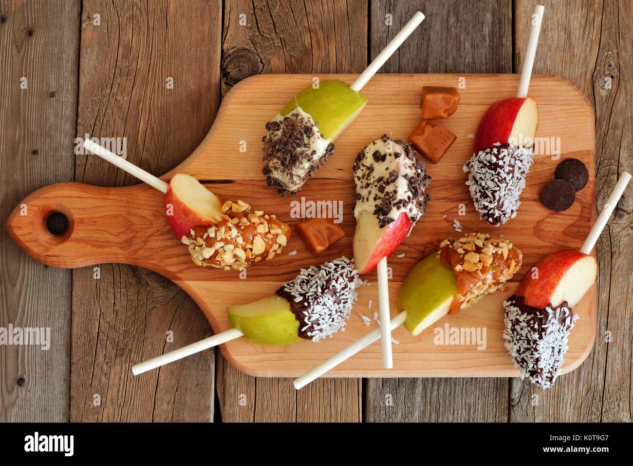 Caramel and chocolate dipped apple slices on a paddle board with rustic wooden background Stock Photo
