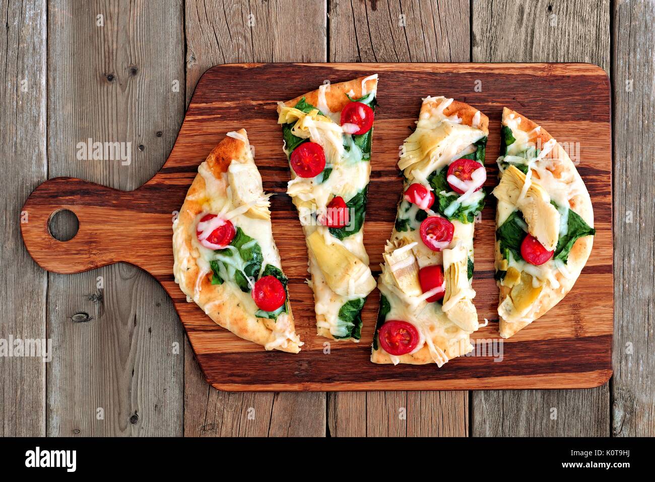 Healthy flat bread pizza with melted mozzarella, tomatoes, spinach and artichokes, above view on