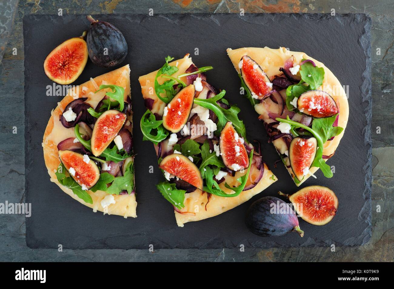 Autumn flat bread pizza with figs, arugula, and goat cheese, overhead scene on slate background Stock Photo