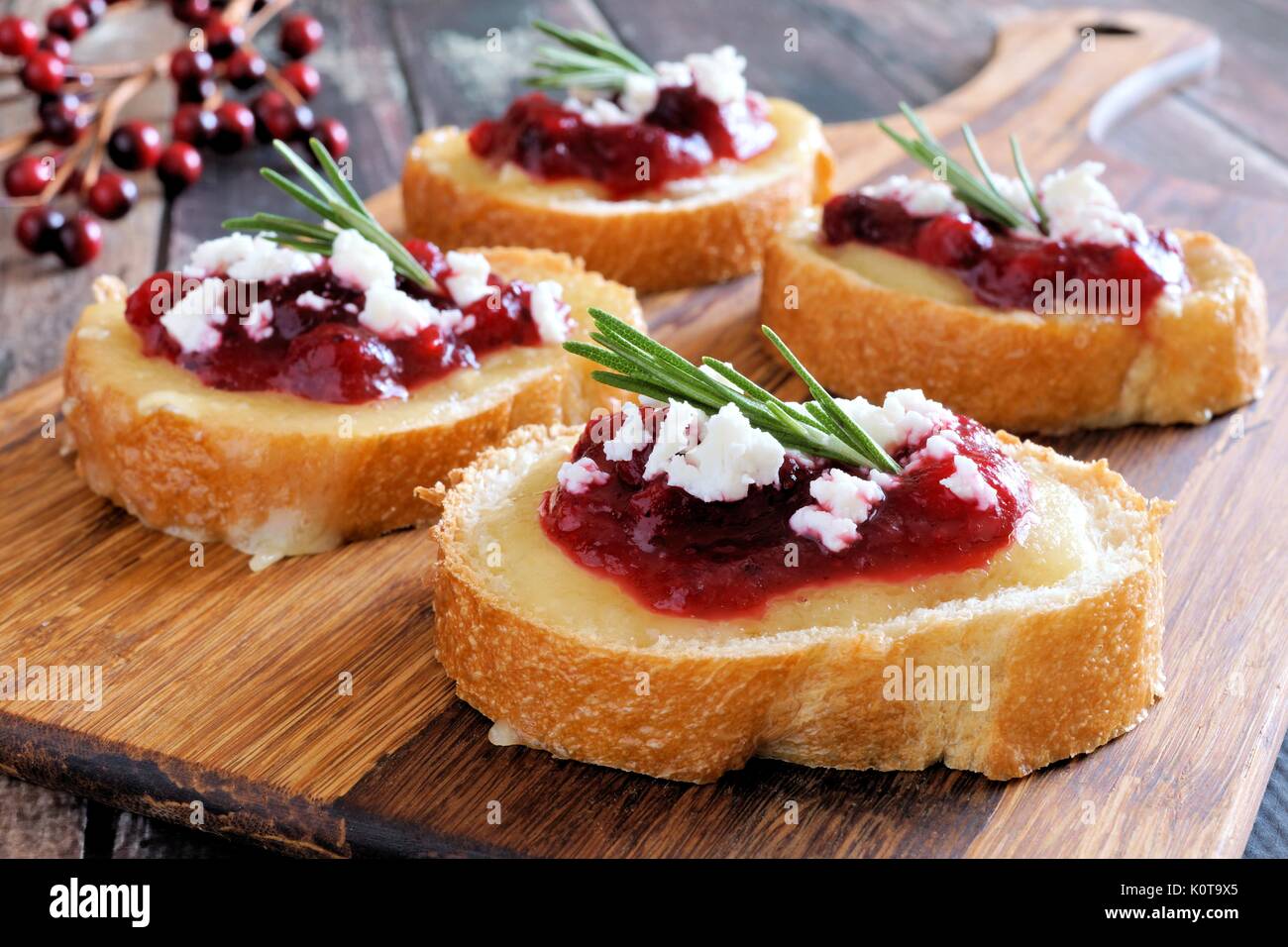 Holiday crostini appetizers with cranberry sauce, brie, feta and rosemary on a wooden server Stock Photo