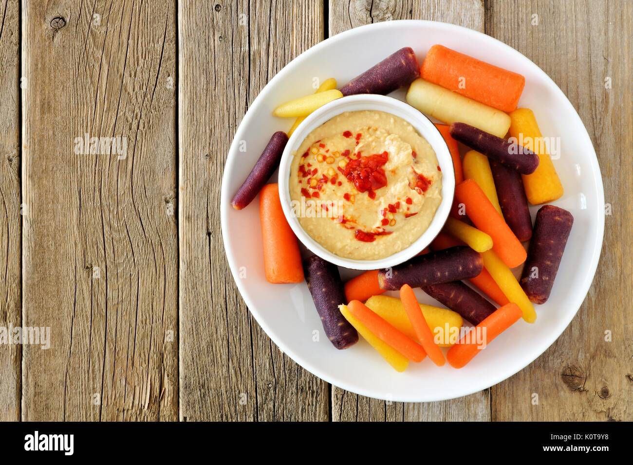 Plate of baby rainbow carrots with hummus dip, overhead view on a rustic wooden background Stock Photo