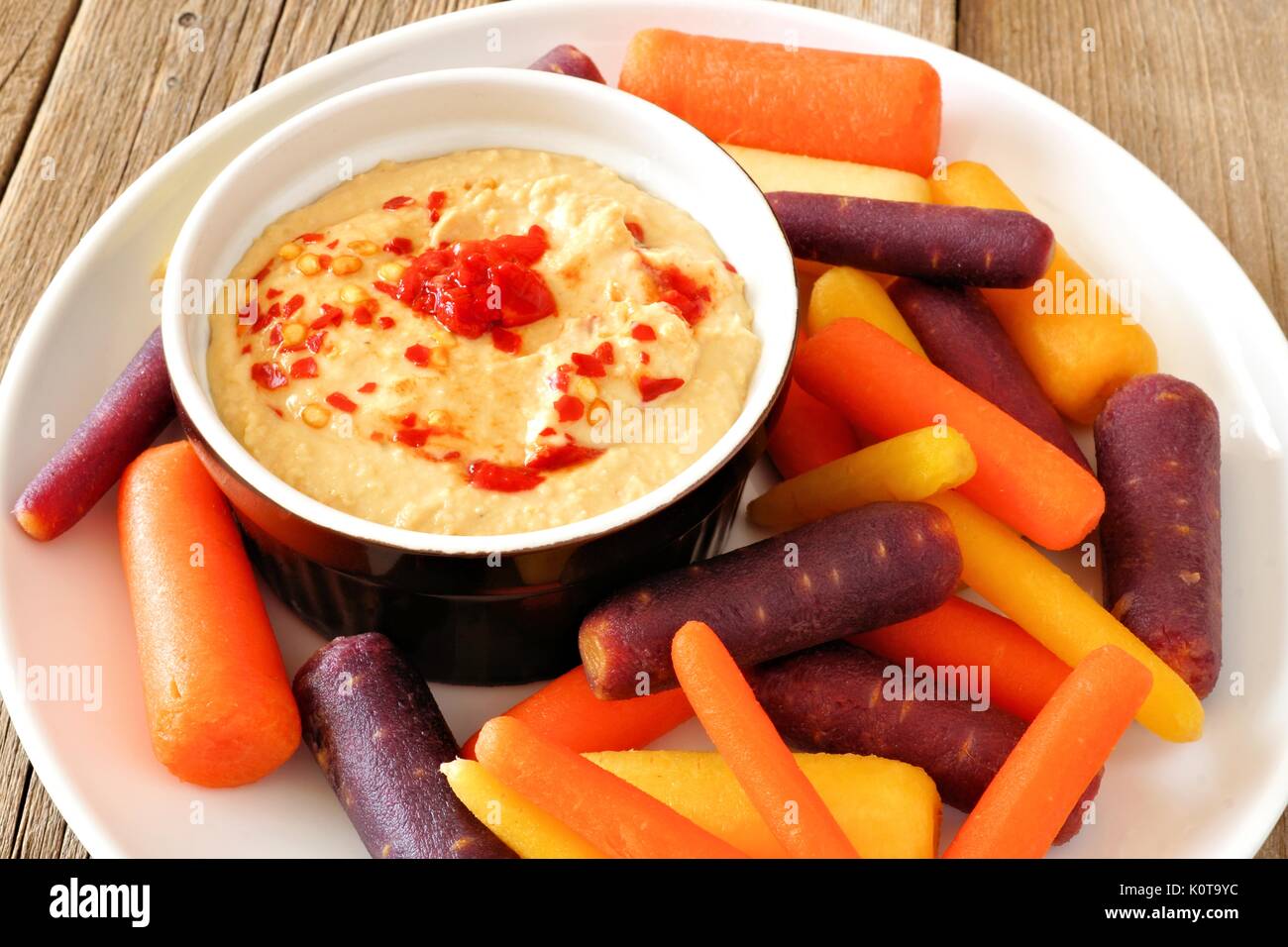 Plate of baby rainbow carrots with hummus dip, close up on a rustic wooden background Stock Photo