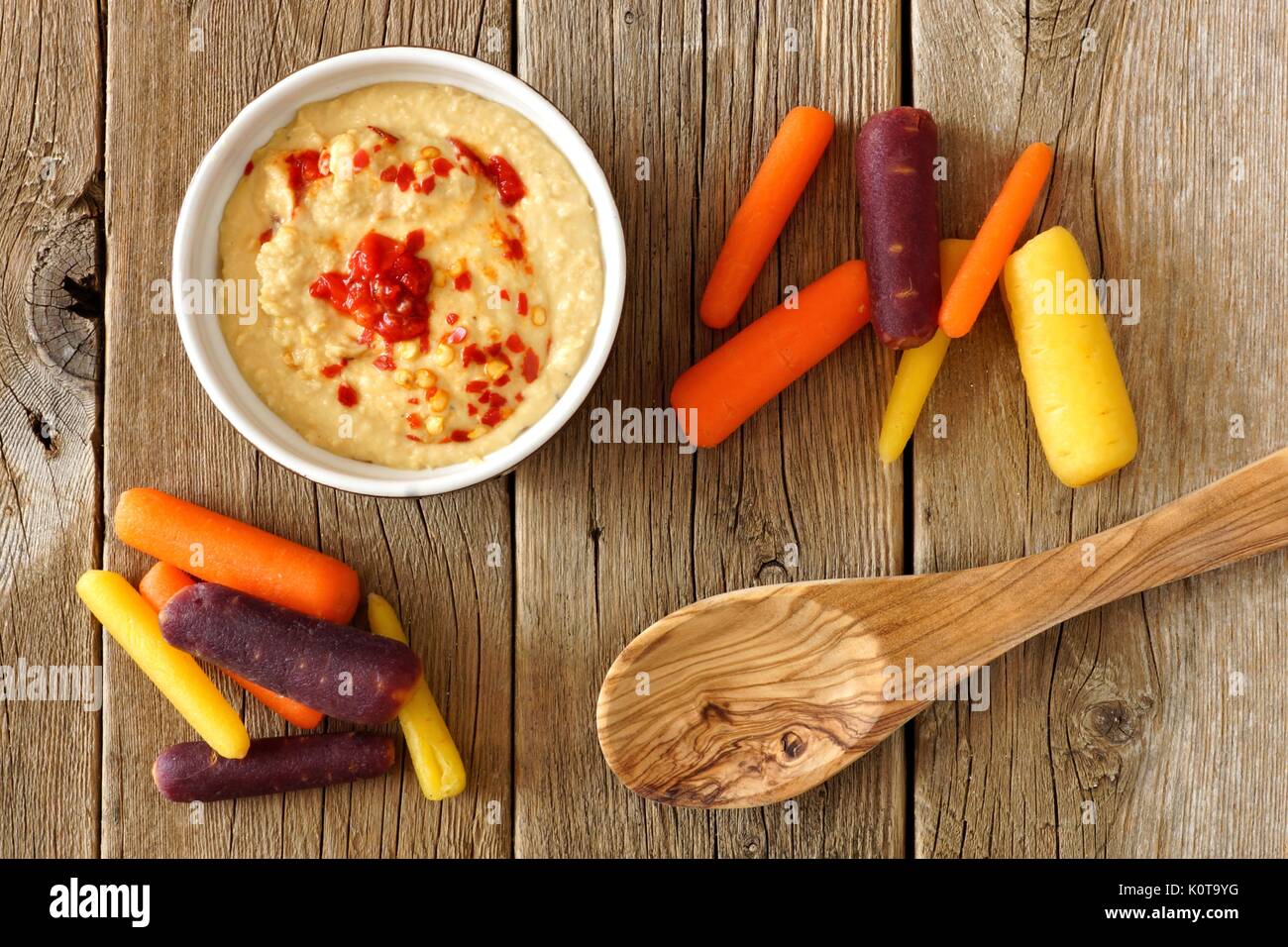Baby rainbow carrots with hummus dip and spoon, overhead view on a rustic wooden background Stock Photo