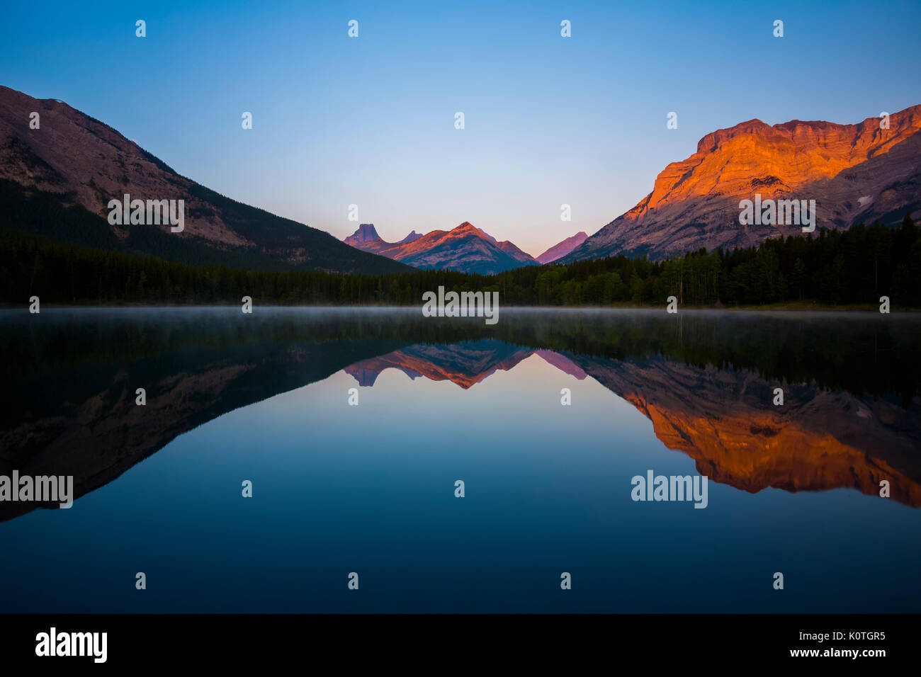 Alpenglow slides down the side of Mount Kidd and neighbouring peaks and is reflected in Wedge Pond in Kananaskis Country. Stock Photo
