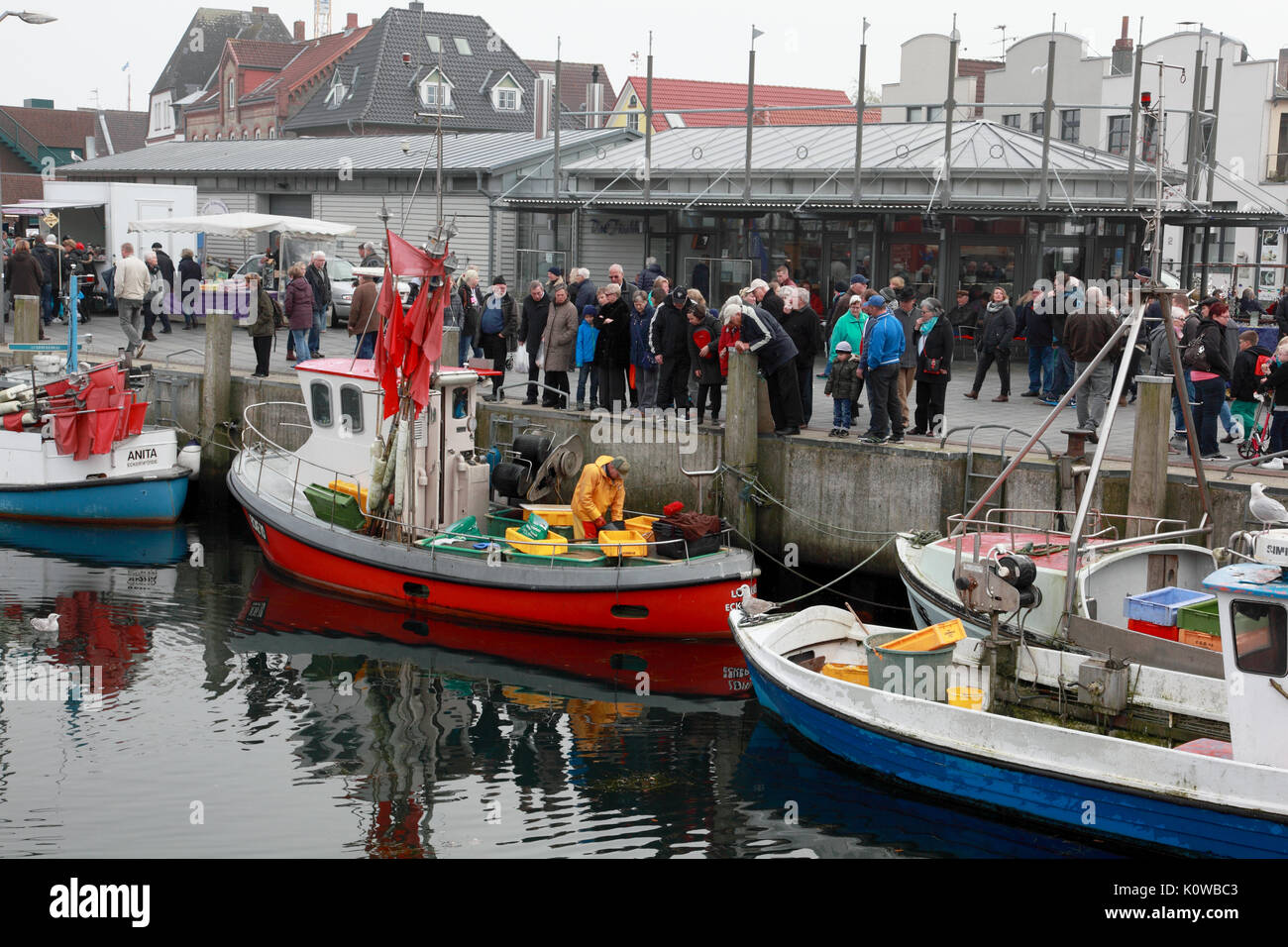 Tourists watching a fisherman at work in Eckernförde old harbour, on the Baltic, in northern Germany, near the Danish border Stock Photo