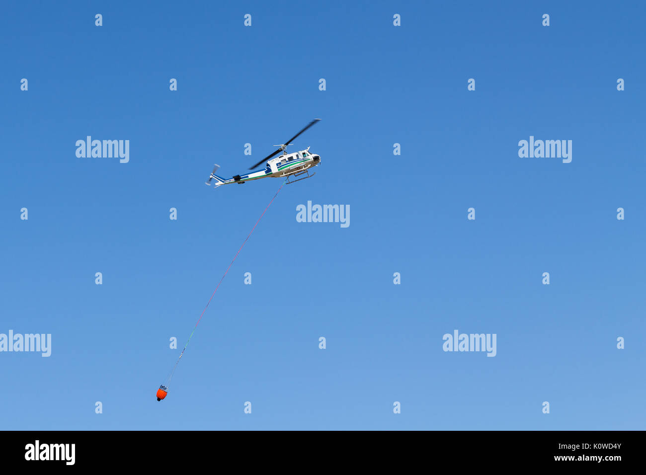 Aerial fire fighting helicopter with red water bucket against blue sky
