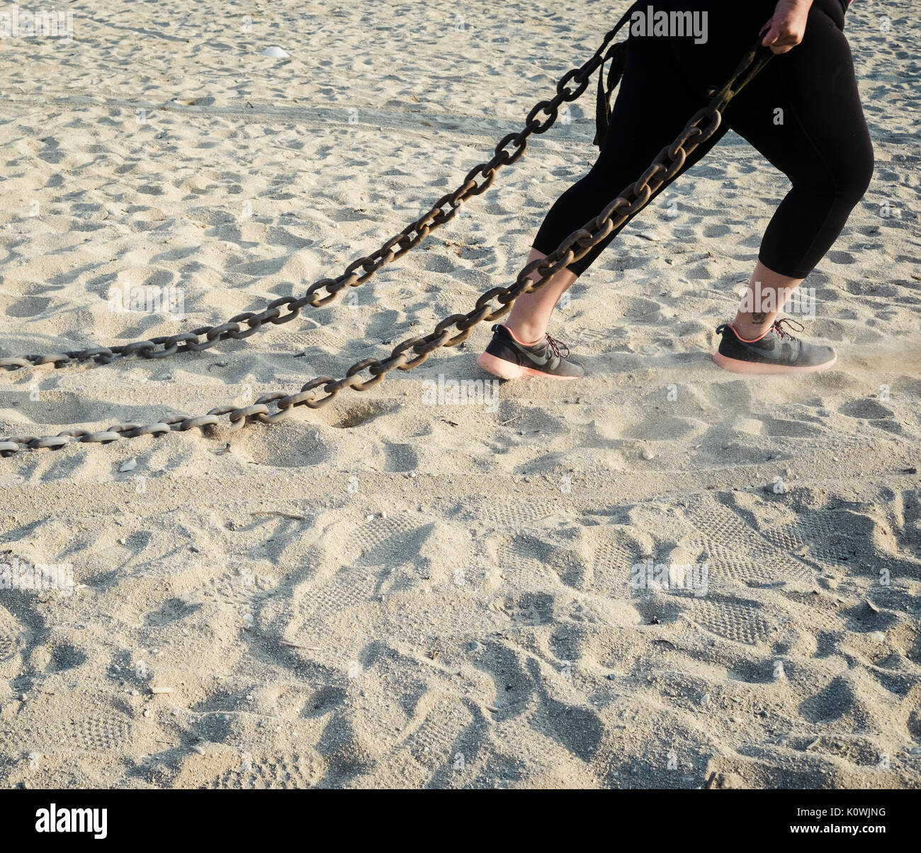 A woman drags a metal chain as part of a bootcamp fitness session on Falmouth's Gyllyngvase Beach. Stock Photo