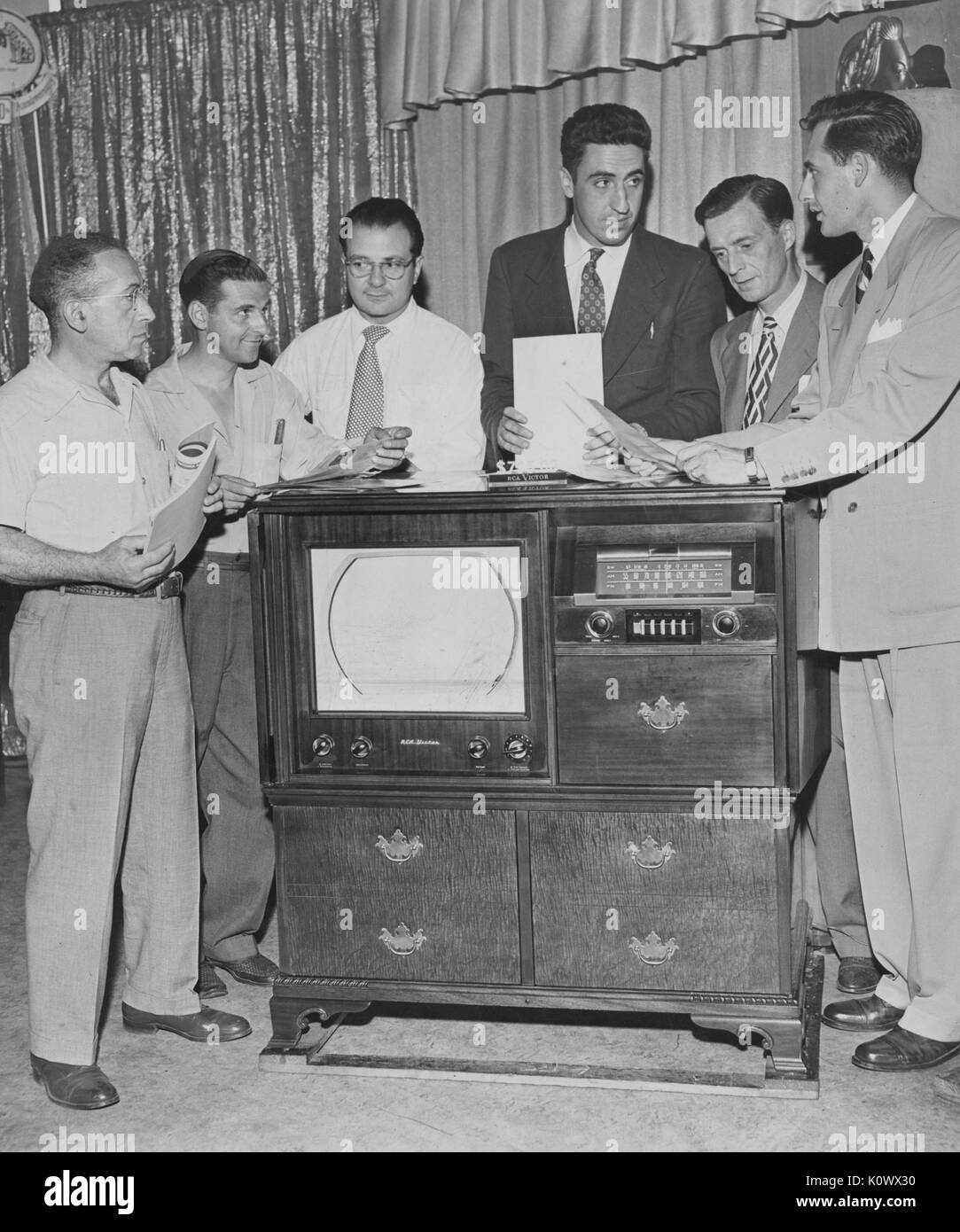 RCA Victor salesmen standing with a model 9TW390 television, reading information about the television during a sales meeting, 1950. Stock Photo
