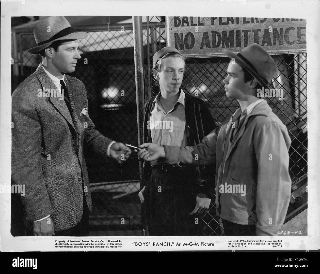 A movie still scene from 'Boys' Ranch' (1946 MGM film), showing two boys and a man outside a fenced area with a 'No Admittance sign, with one of the boy handing over something to the man, 1946. Stock Photo