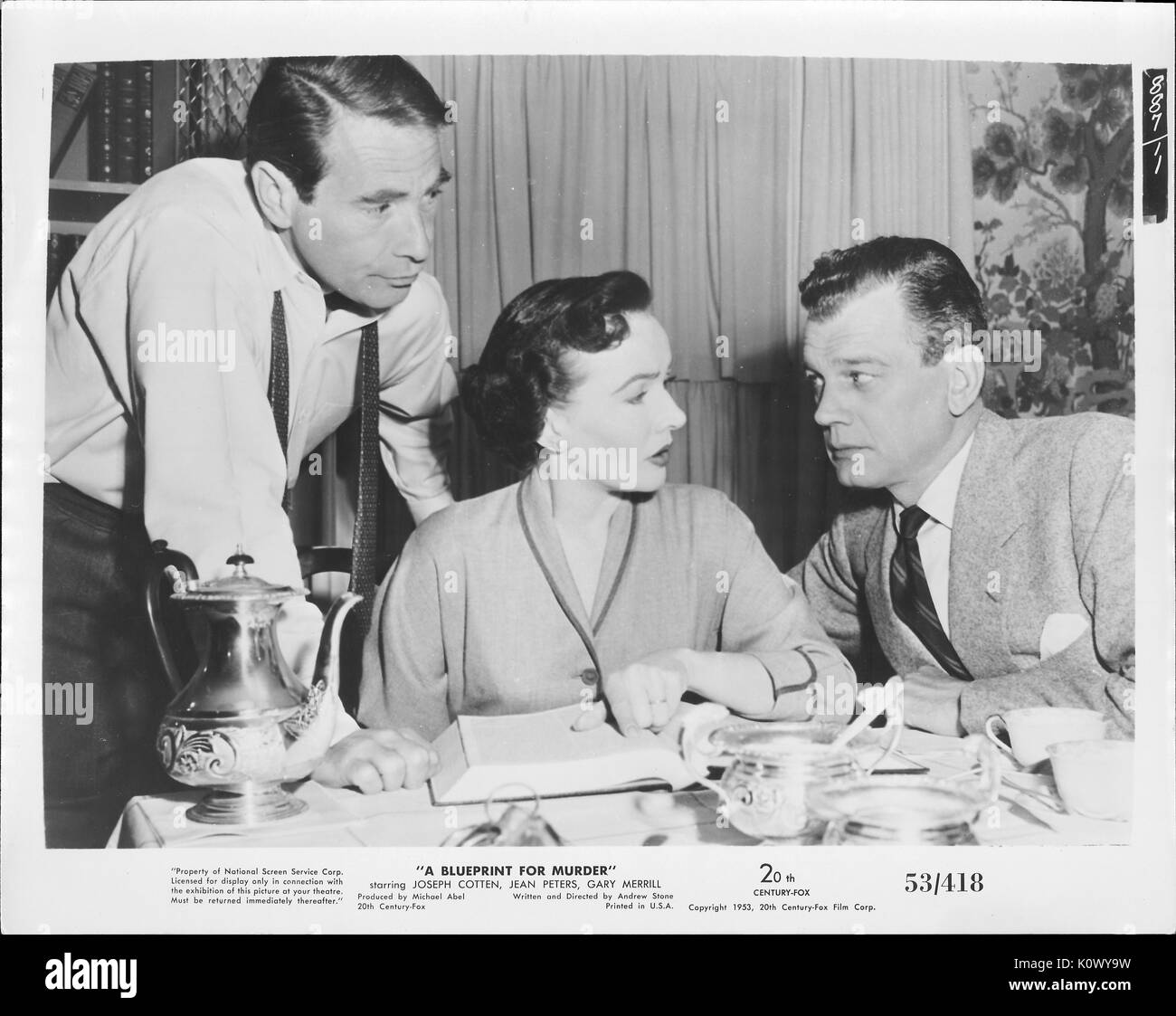 A movie still scene from 'A Blueprint For Murder' (1953 20th Century Fox thriller film), showing a seated woman pointing out something in a book to the man on her left while the other man on her right listens, 1953. Stock Photo