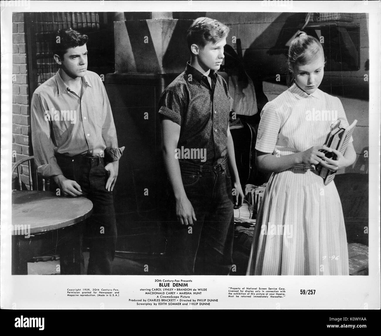 A movie still scene from 'Blue Denim' (1959 20th Century Fox film), showing  three serious-looking teenagers standing about, a girl and two boys, with  the girl looking down while listening to the