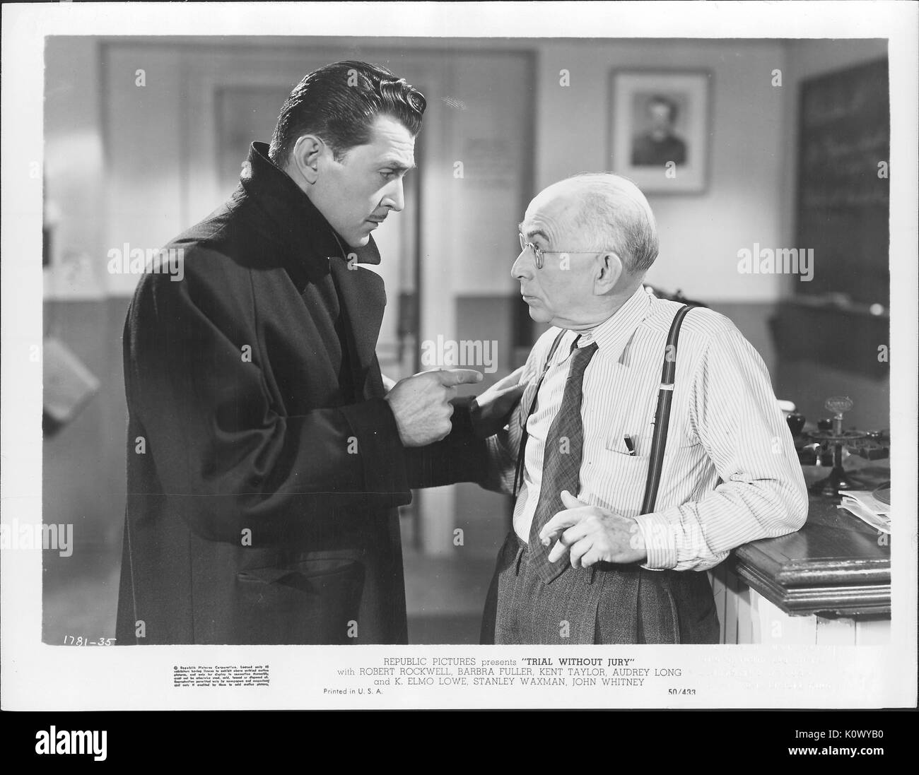 A movie still scene from 'Trial Without Jury' (1950 Republic Pictures mystery film), showing a handsome man in dark suit squatting seemingly admonishing a cigar-smoking bespectacled old man wearing a striped long-sleeved shirt with a tie and suspenders, 1950. Stock Photo