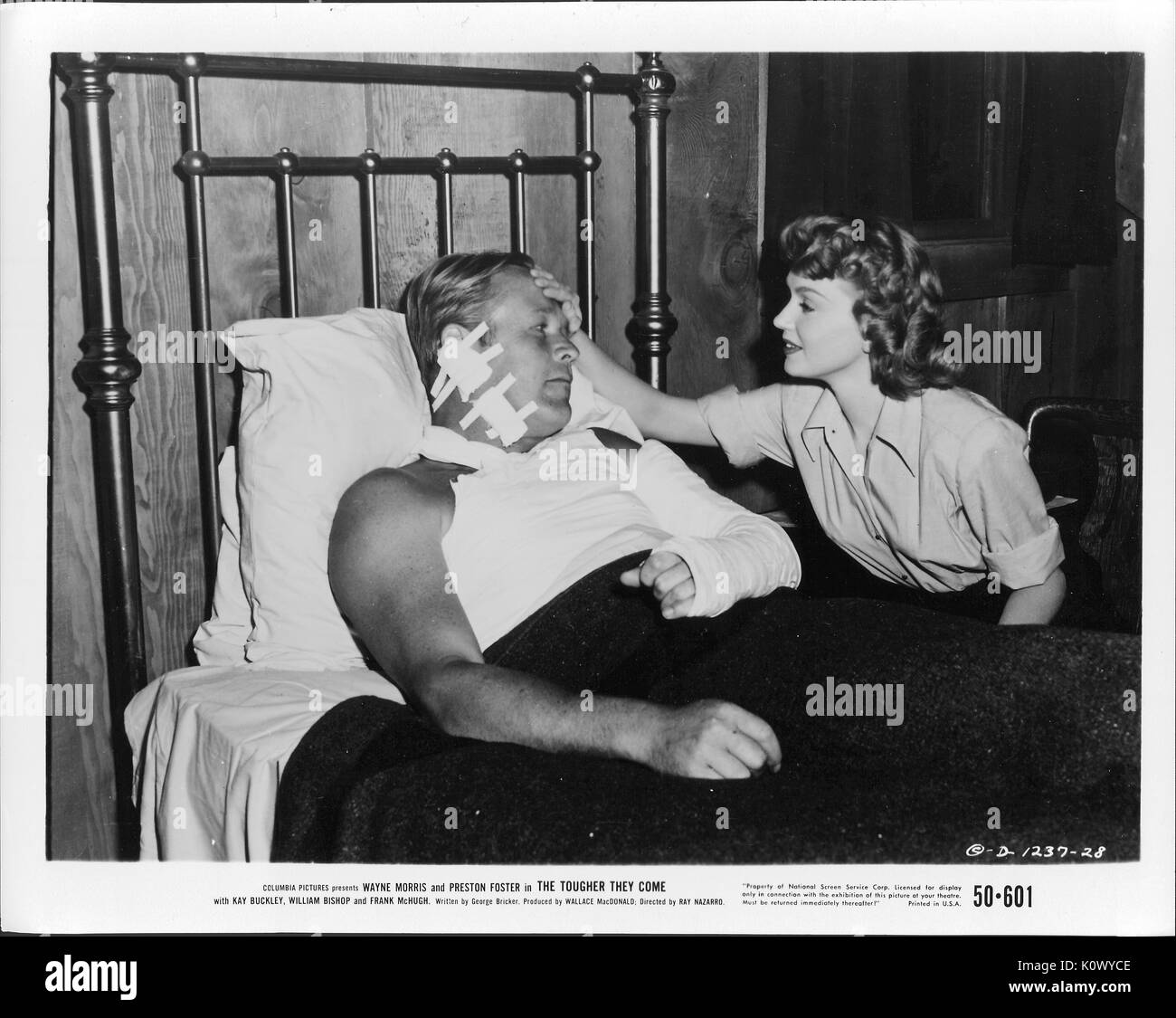 A movie still scene from 'The Tougher They Come' (1950 Columbia Pictures film), showing an injured man with bandages on the left side of his head and his left arm in a cast lying in bed while a young woman puts her right hand on his forehead to check his temperature, 1950. Stock Photo
