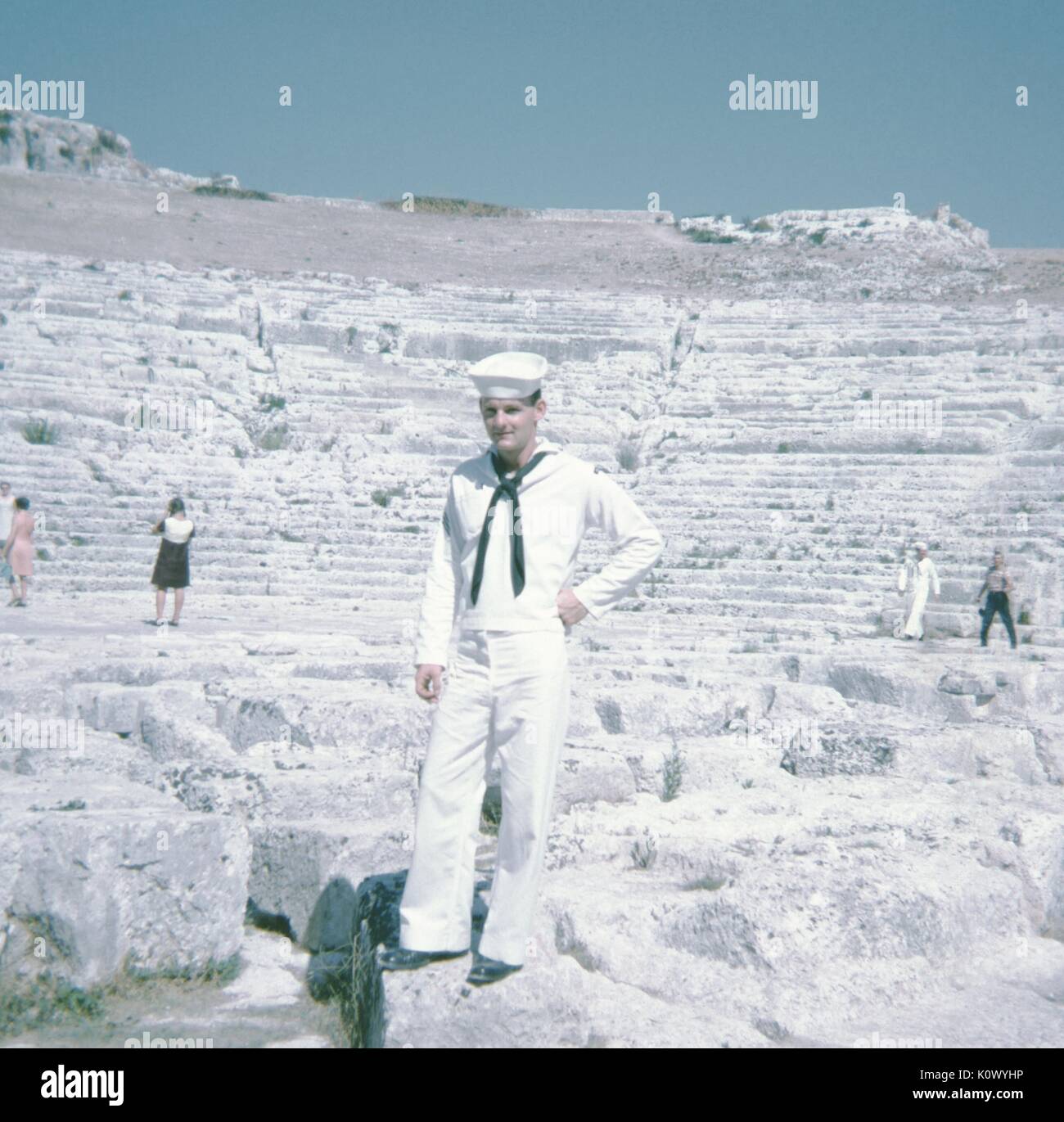 Sailor in United States Navy uniform, standing with his hands on his hips in front of the ruins of a Roman amphitheatre, other tourists in the background using cameras to take photographs, Athens, Greece, 1967. Photo credit Smith Collection/Gado/Getty Images. Stock Photo