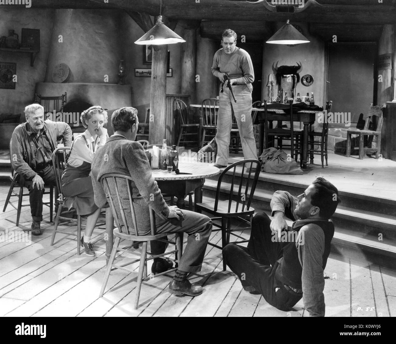 Bette Davis and other actors in a Western movie still, sitting around a table in a home, a man with a shotgun threatening the group, a second man on the floor, knocked out of his chair, reaching for a pistol in his vest, 1949. Photo credit Smith Collection/Gado/Getty Images. Stock Photo