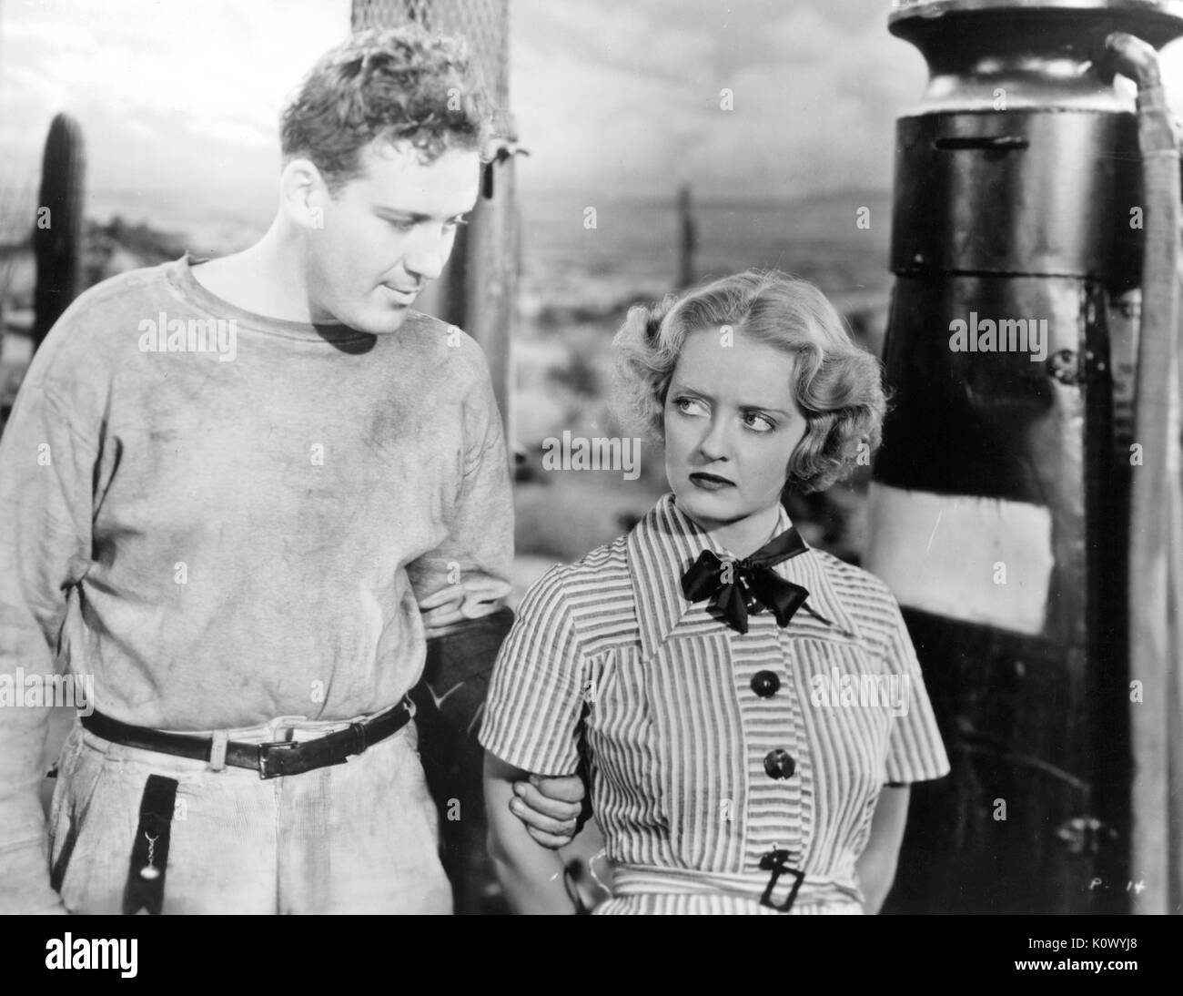 Bette Davis and unidentified man standing together near a gasoline pump, Davis with an angry expression, in a movie still, 1949. Photo credit Smith Collection/Gado/Getty Images. Stock Photo