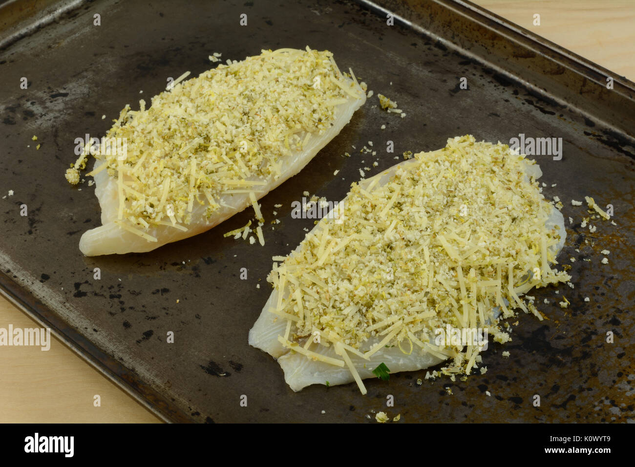 Two raw tilapia fish fillets with parmesan cheese and bread crumb topping on baking sheet Stock Photo