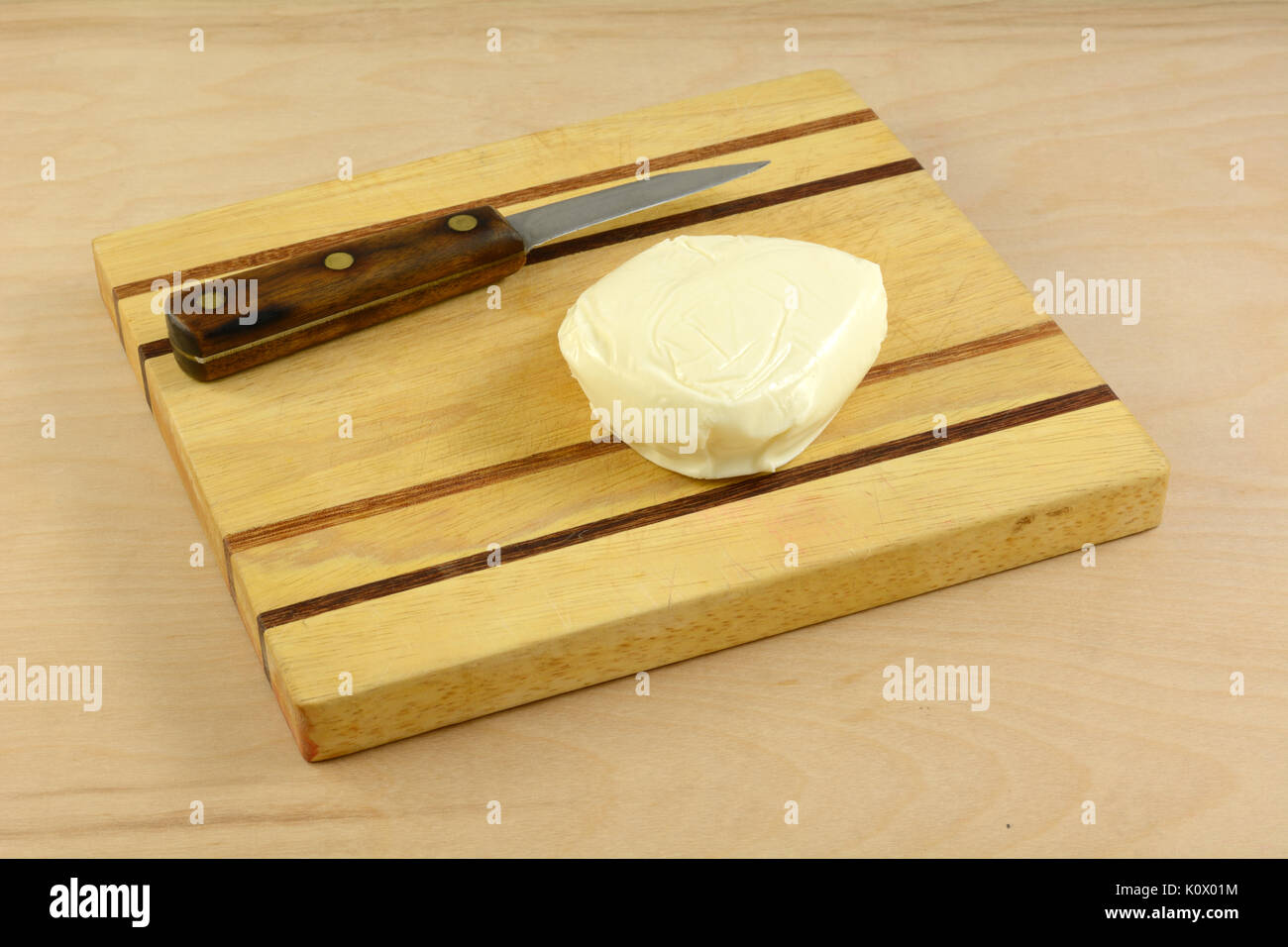 Whole ball of fresh mozzarella cheese on wooden cutting board with knife Stock Photo