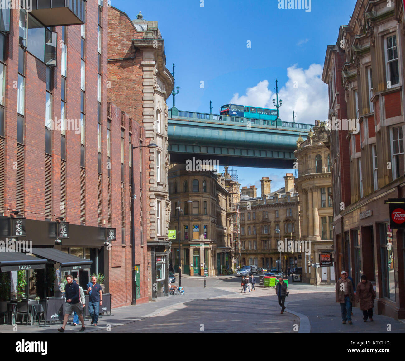 Section of Tyne River bridge and double decker bus passing across tops of city buildings and street under blue sky at Newcastle-upon-Tyne, England Stock Photo