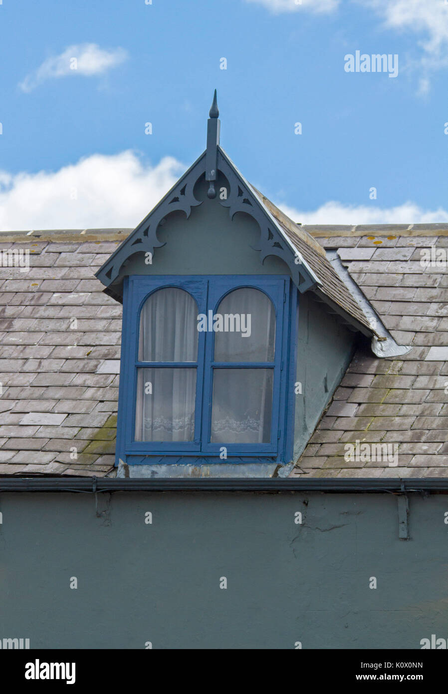 Dormer window with blue painted frame in slate roof of English house against blue sky Stock Photo