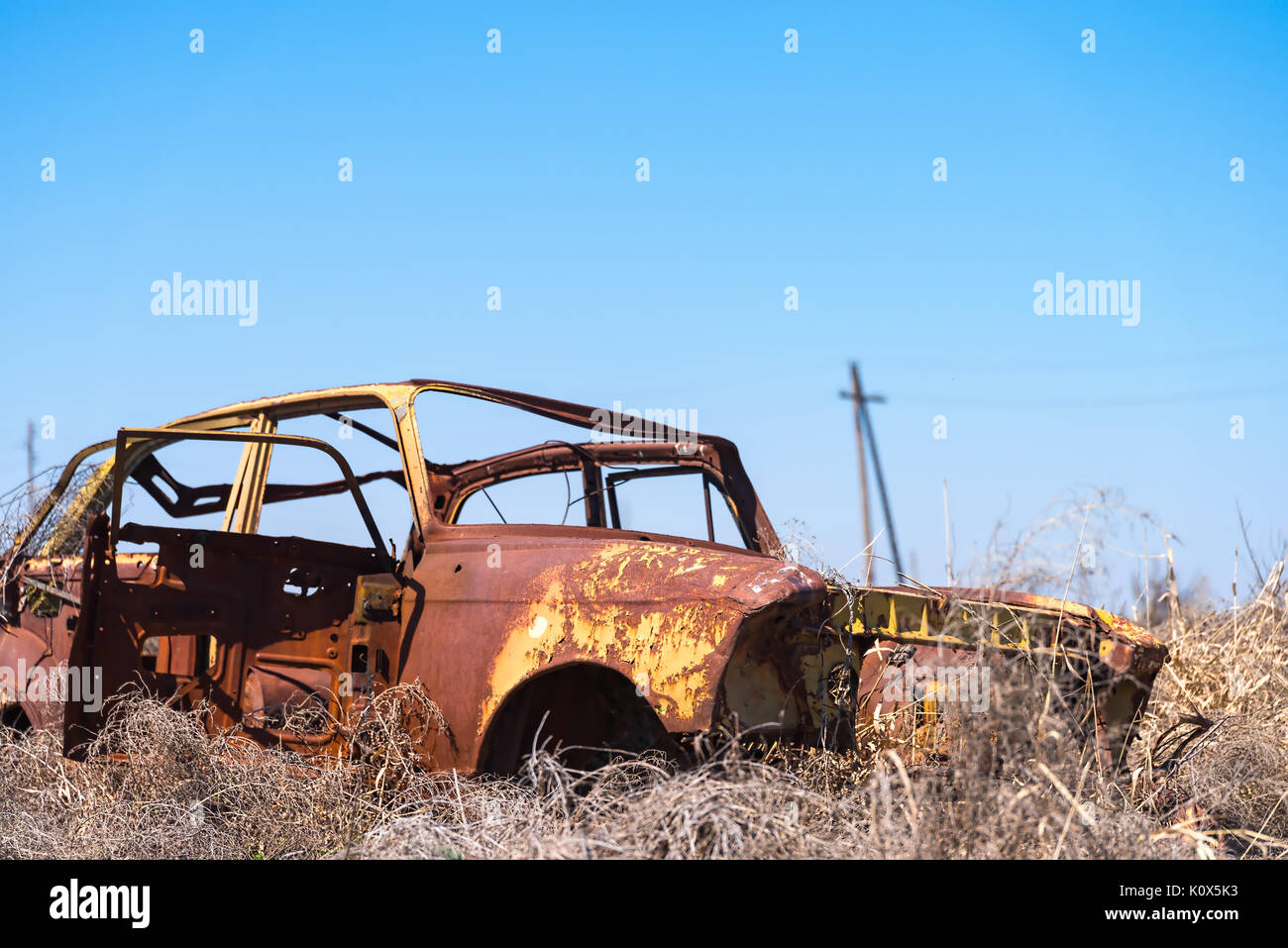 Abandoned and rusty wreckage of an yellow vintage Soviet Russian car in the middle of dry hay with scenic ice top mountains in Southern Armenia Stock Photo
