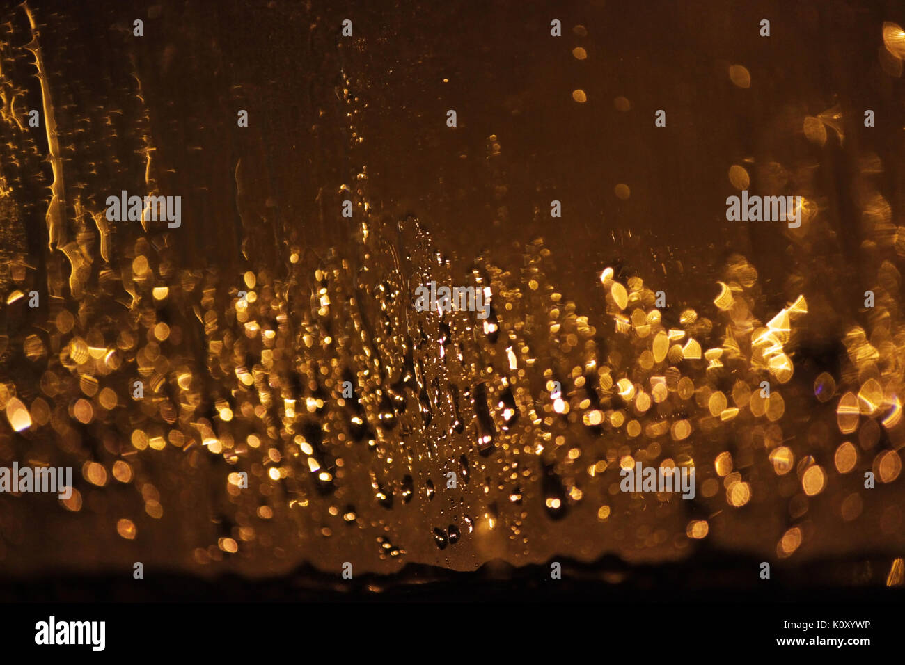 Drops of night rain on a glass of golden color, light of lanterns ...