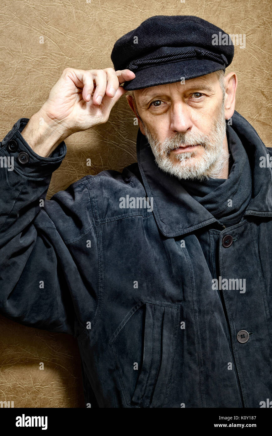 Portrait of a mature man with a white beard adjusting his cap on the head. He could be a sailor, a worker, a docker, or even a gangster or a thug. He  Stock Photo