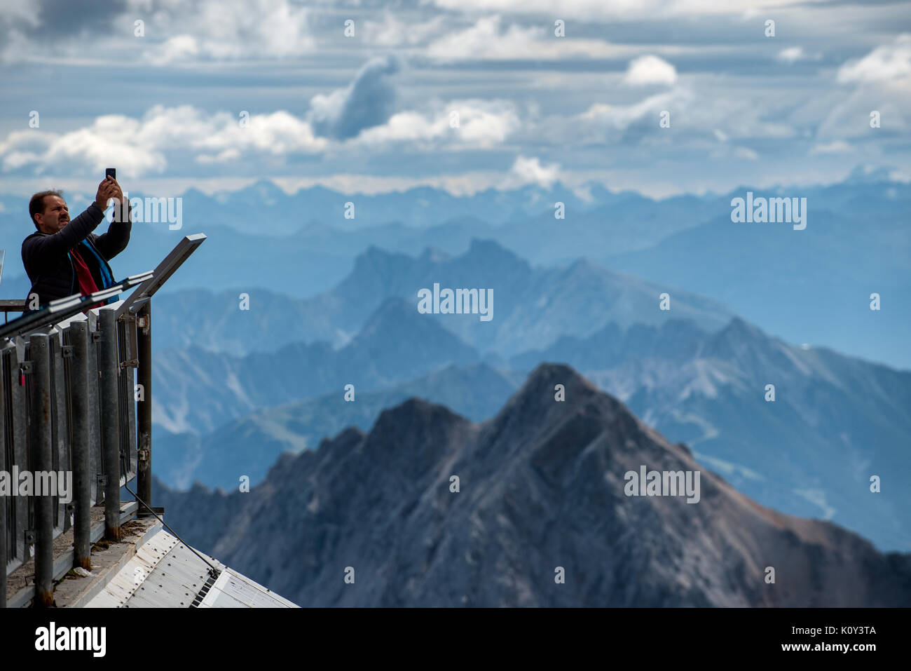 A man takes a selfie with a smart phone at the summit of the Zugspitze mountain on the Germany-Austria border. Stock Photo